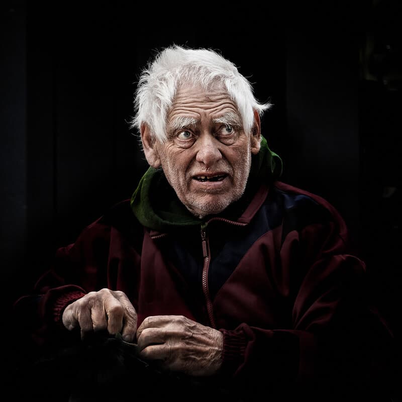 An elderly man sitting in a dark room.