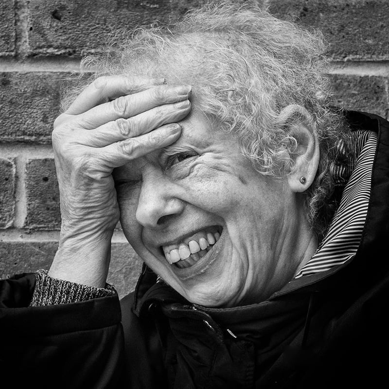 A black and white photo of an old woman laughing.