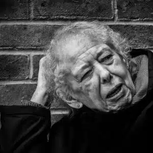 An old woman leaning against a brick wall.