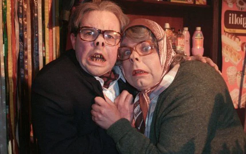 A man and woman in glasses are hugging each other.