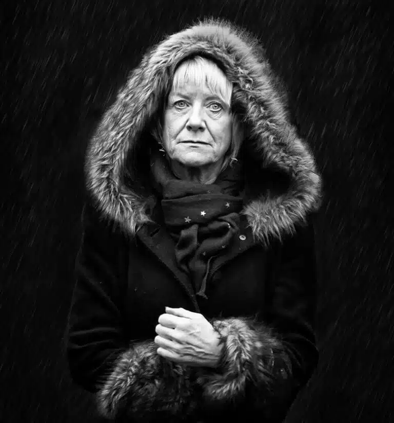 Faces_Photo_by John Gill-35 A black and white photo of an older woman in the rain.