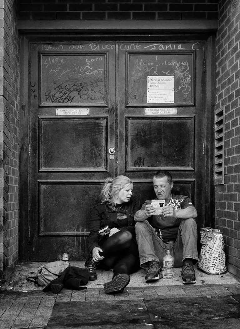 Black and white photograph of a man and woman sitting outside a door.