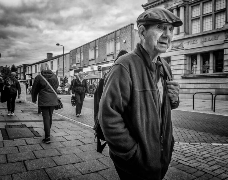 A black and white photo of an old man walking down the street.
