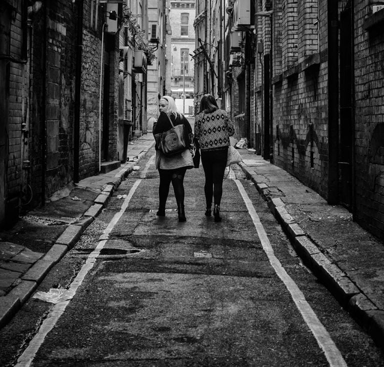 Two people walking down an alley in black and white.