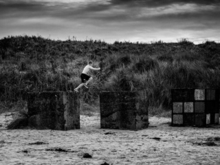 A man is jumping over concrete blocks on the beach.