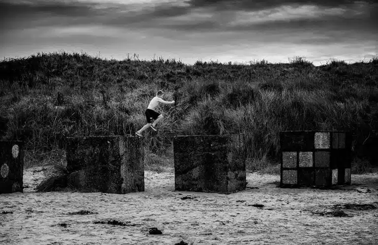 A man is jumping over concrete blocks on the beach.