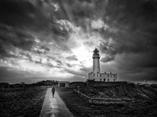 A black and white photo of a lighthouse under a stormy sky.