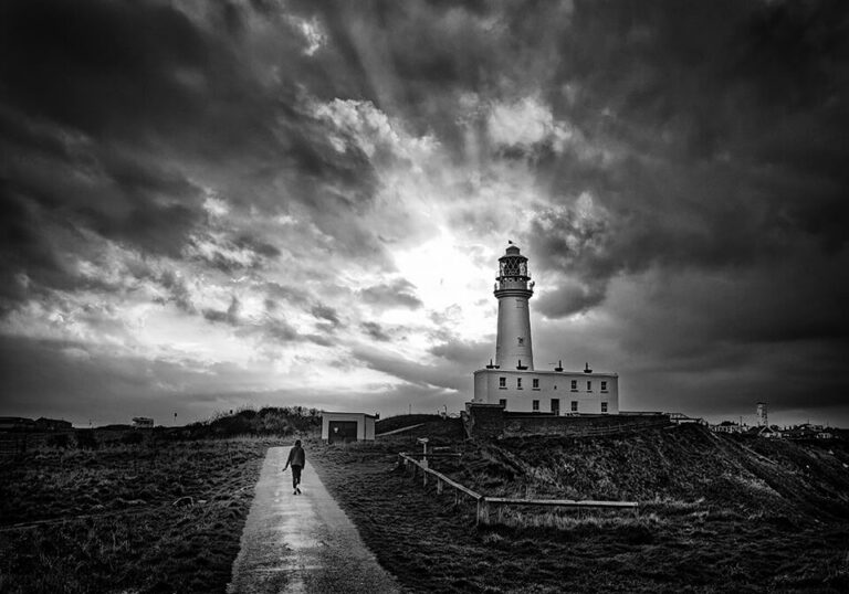 A black and white photo of a lighthouse under a stormy sky.