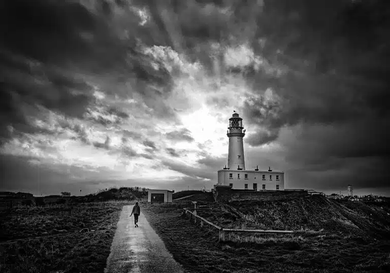 A black and white photo of a lighthouse under a stormy sky.