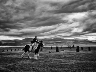A man riding a horse in a field under a cloudy sky.