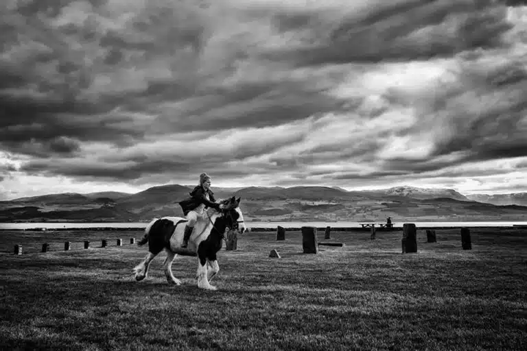 A man riding a horse in a field under a cloudy sky.