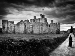 A black and white photo of a person walking down a path in front of a castle.