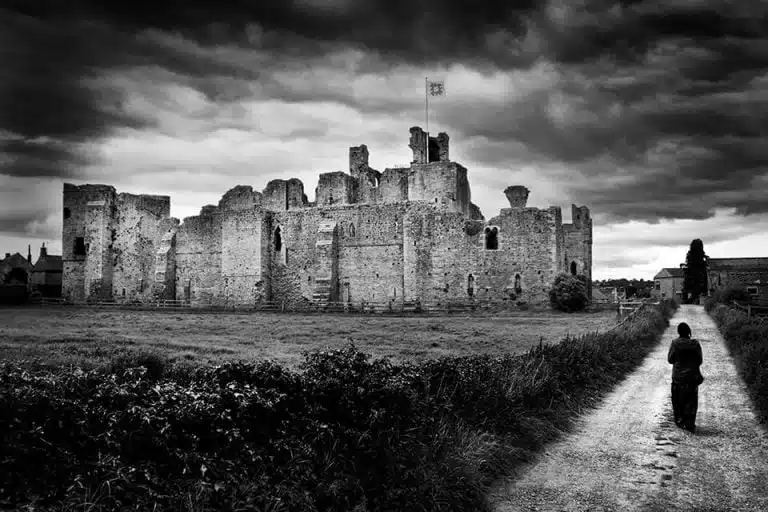 A black and white photo of a person walking down a path in front of a castle.