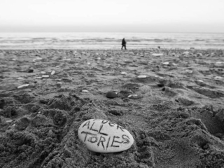 A black and white photo of a person standing on a rock in the sand.