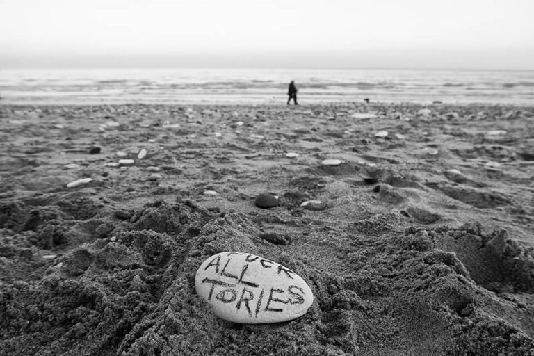 A black and white photo of a person standing on a rock in the sand.