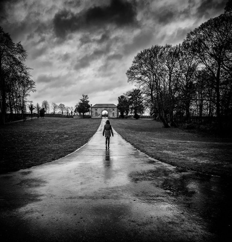 A black and white photo of a person walking down a path.