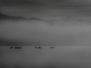 A black and white photo of a group of boats on a lake.