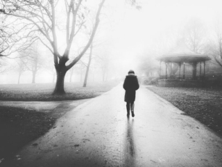A black and white photo of a person walking in a park.