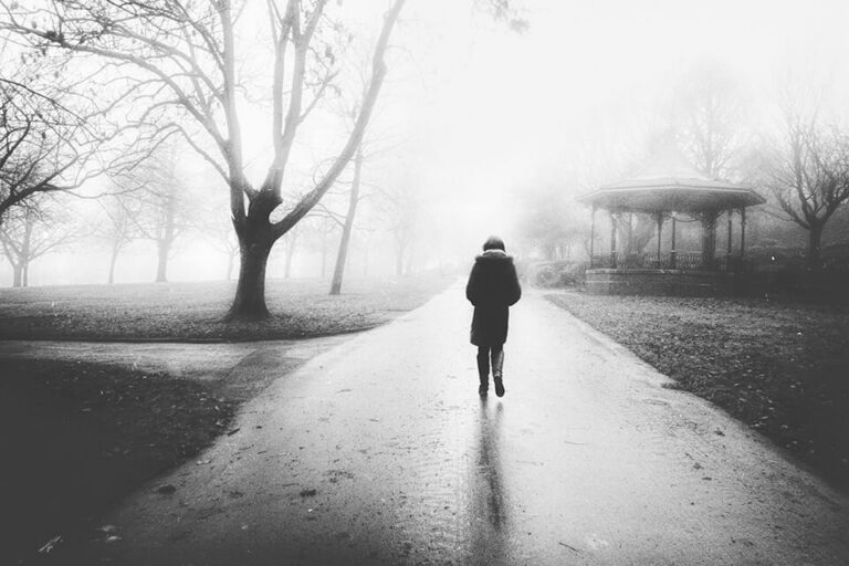 A black and white photo of a person walking in a park.