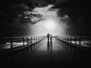 Two people standing on a pier under a stormy sky.
