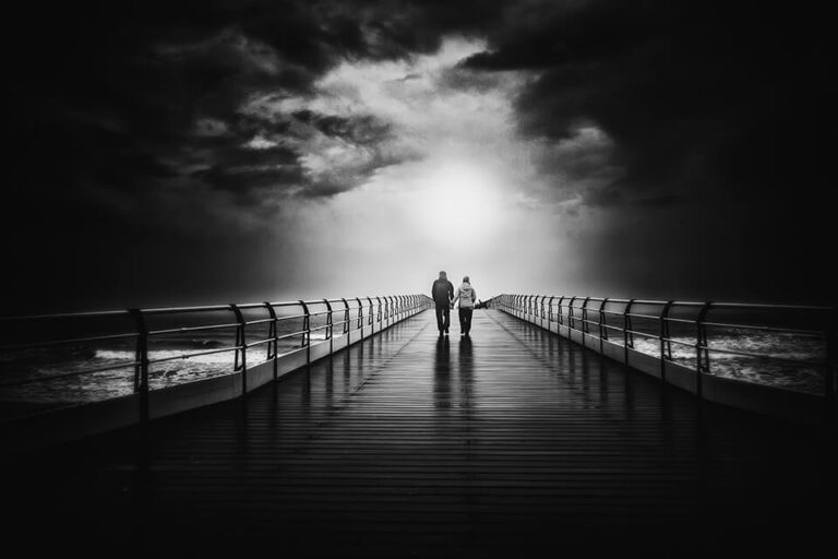 Two people standing on a pier under a stormy sky.