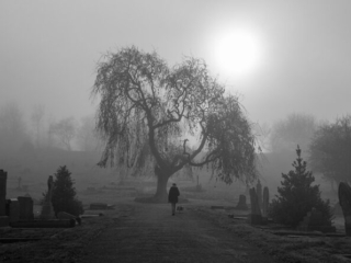 A black and white photo of a person walking through a cemetery.
