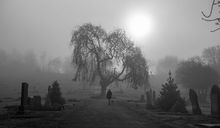 A black and white photo of a person walking through a cemetery.