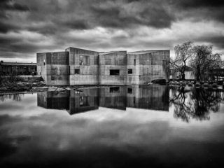 A black and white photo of a concrete building reflected in water.
