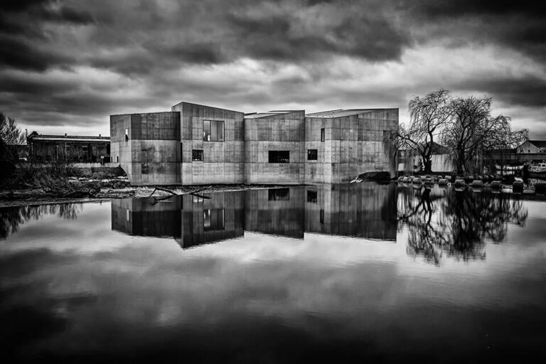 A black and white photo of a concrete building reflected in water.