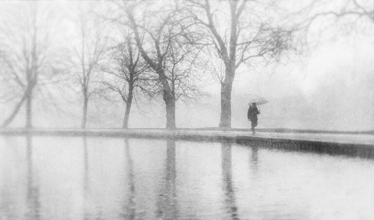 A black and white photo of a person walking by a pond.