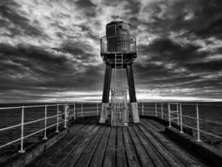 A black and white photo of a lighthouse on a pier.