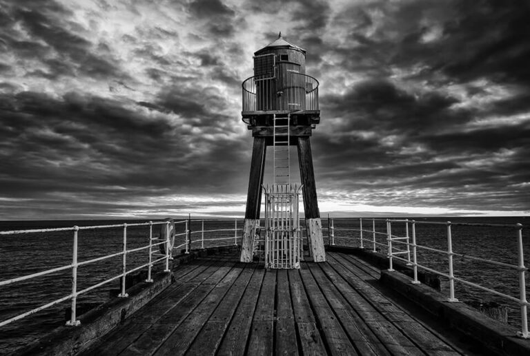A black and white photo of a lighthouse on a pier.