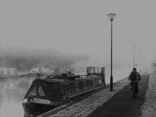 A person is riding a bike on a sidewalk next to a boat.