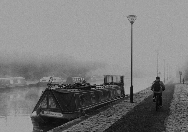 A person is riding a bike on a sidewalk next to a boat.