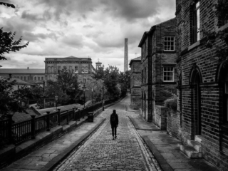 A black and white photo of a man walking down a cobblestone street.