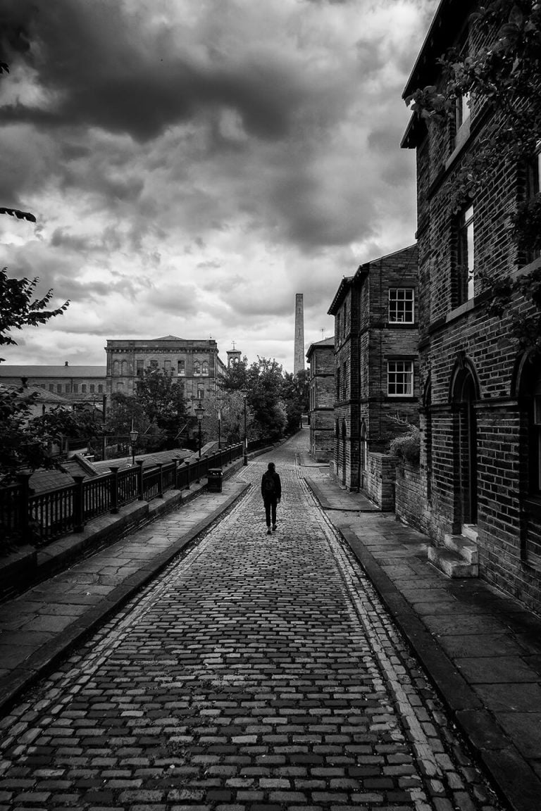 A black and white photo of a man walking down a cobblestone street.