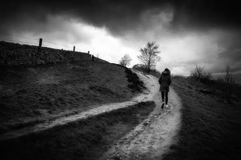 A black and white photo of a person walking down a path.