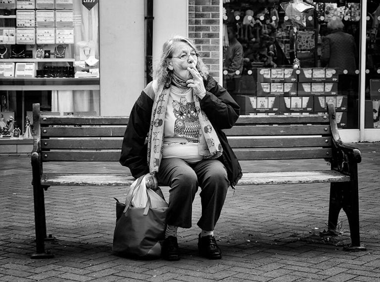 Redcar street photograph-08 A woman sitting on a bench smoking a cigarette.