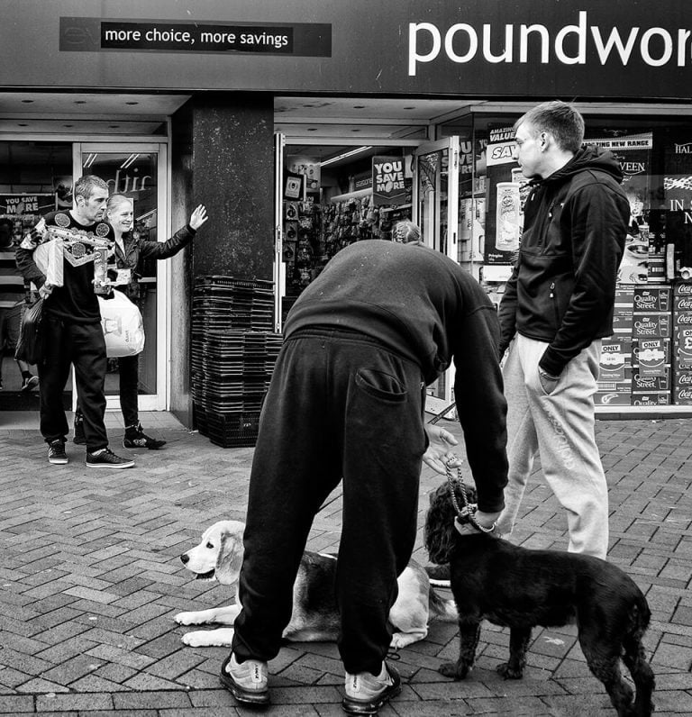 Redcar street photograph-09 A man is petting a dog in front of a store.