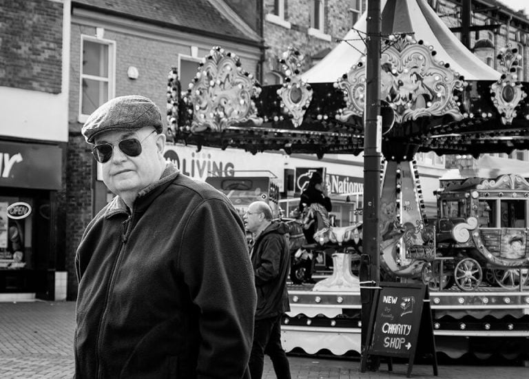 Redcar street photograph-13 An old man standing in front of a carousel.