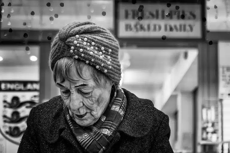 Street_Photography_Leeds_by John Gill-12 An old woman in a hat is looking at her phone.