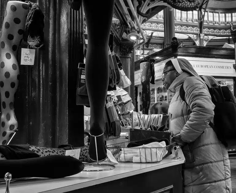 Street_Photography_Leeds_by John Gill-14 Black and white photo of a woman looking at clothes in a market.