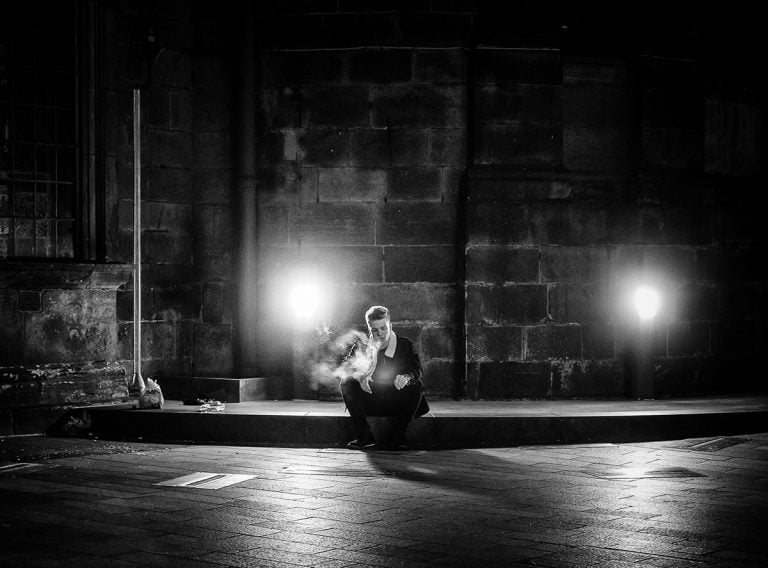 A black and white photo of a man sitting on the ground at night.