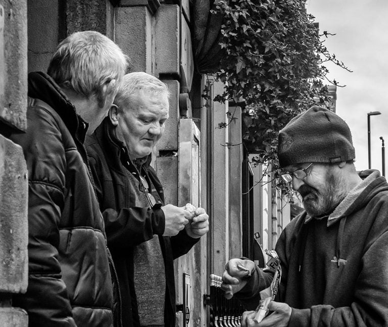 Three men standing on a street talking to each other.