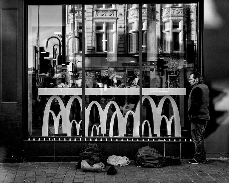 A black and white photograph of a man sitting in front of a mcdonald's.