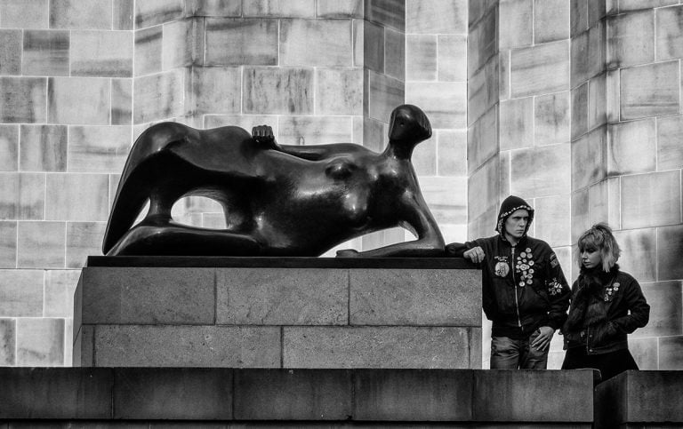 Two people standing next to a sculpture in front of a building.