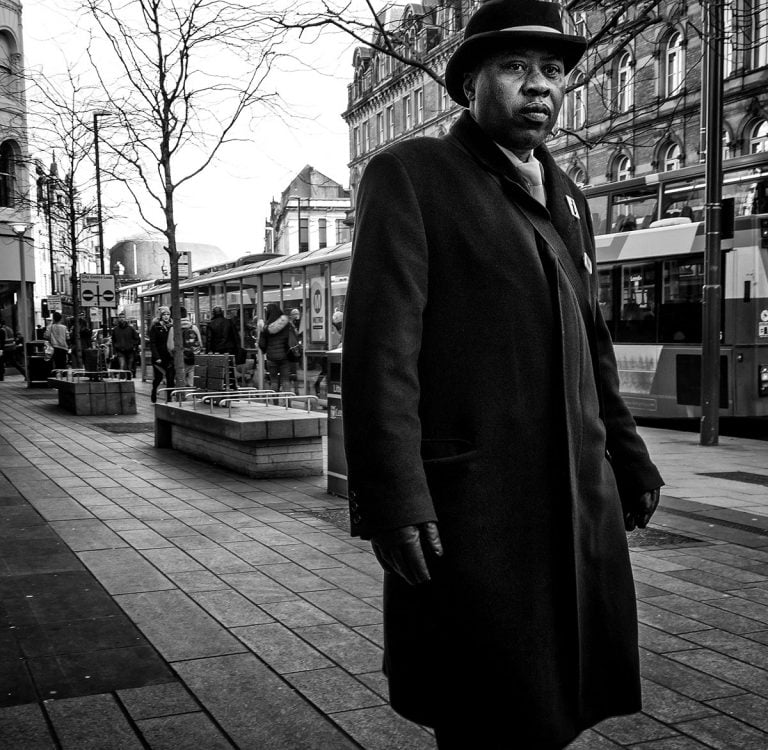 A man in a coat and hat standing on a sidewalk.