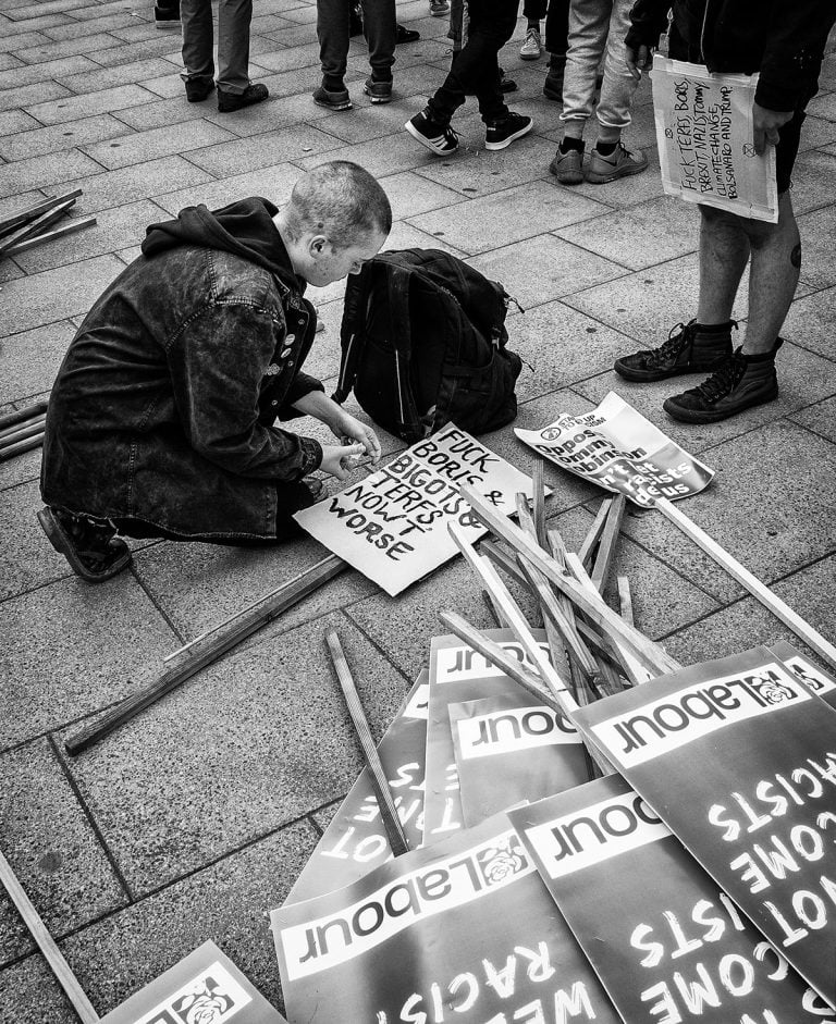 A man kneeling on the ground with signs in front of him.