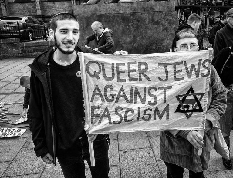 A group of people holding a sign that says queer jews against fascism.