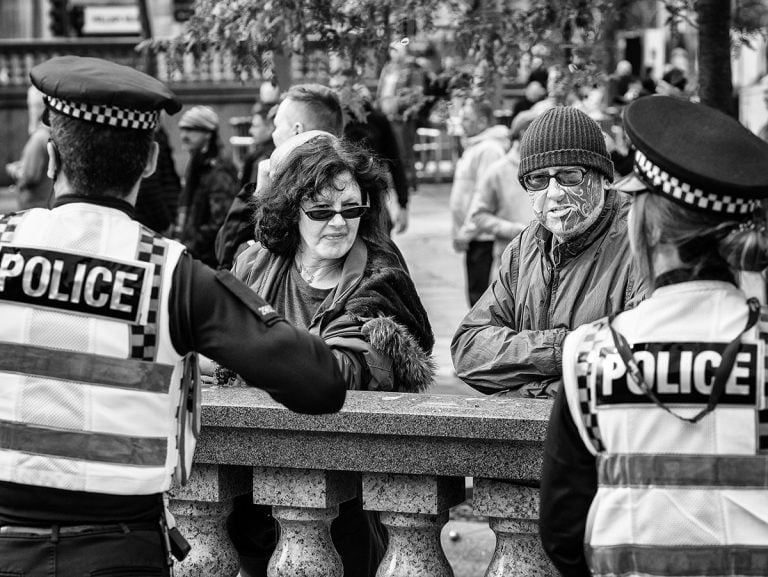 A black and white photo of a group of people talking to a police officer.